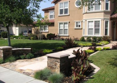 elegant front yard walkway with stone pillars and greenery designed by residential landscape contractor